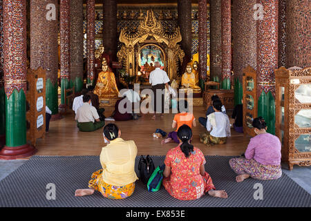 People meditating in front of Buddha statues, Shwedagon Pagoda, Yangon, Myanmar Stock Photo