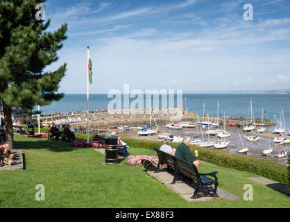 Groups of people seated on benches and overlooking the harbour at New Quy, Ceredigion, Wales Stock Photo
