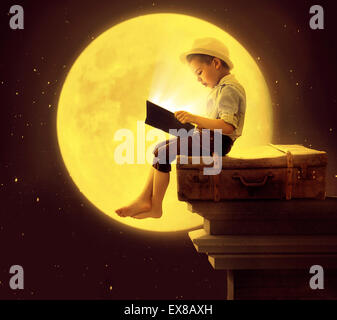 Cute little kid reading a book in the moon light Stock Photo