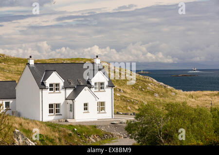 A modern house in Tarbert on the Isle of Harris, Outer Hebrides, Scotland, UK, with the ferry sailing out to sea behind. Stock Photo