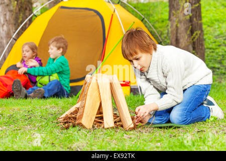 Boy prepares bonfire in forest with other children Stock Photo