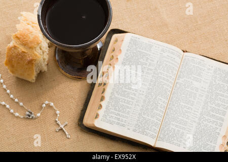 High angle view of open Holy Bible, pearl rosary beads, piece of bread and chalice with wine Stock Photo