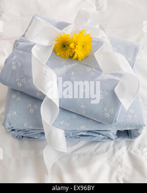 Stack of bedding set with white ribbon and yellow flower head Stock Photo