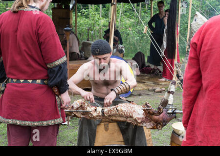 A man at a medieval festival carves a pig roast on a spit Stock Photo