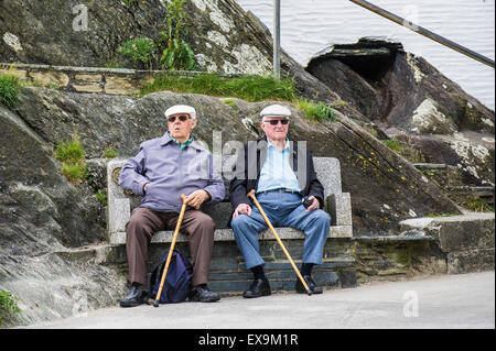 Two elderly holidaymakers sitting on a bench in the harbour in Polperro, Cornwall. Stock Photo