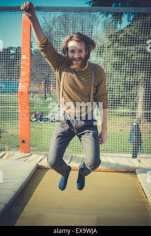 young bearded stylish handsome hipster man jumping on trampoline at playground Stock Photo