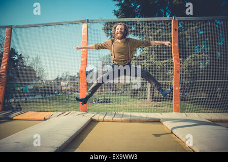 young bearded stylish handsome hipster man jumping on trampoline at playground Stock Photo
