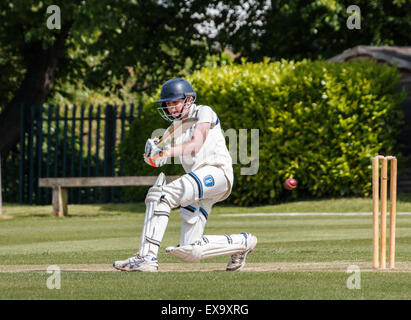 A teenage batsman plays a shot whilst batting during a school cricket match. He is wearing full cricket gear and is one knee hitting the cricket ball