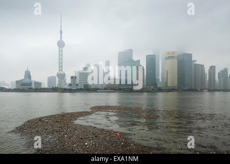 China, Shanghai, Vast pool of trash floats past skyline of Pudong District beneath low clouds along Huangpu River on winter morn Stock Photo