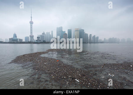 China, Shanghai, Vast pool of trash floats past skyline of Pudong District beneath low clouds along Huangpu River on winter morn Stock Photo