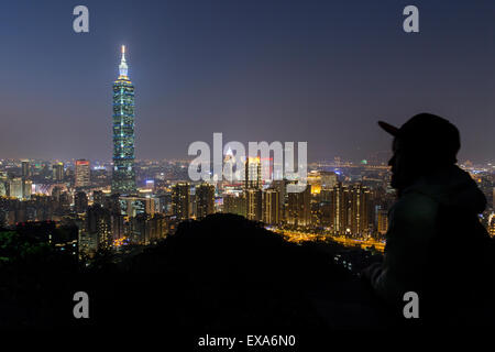 Asia, Taiwan, Taipei, Silhouette of visitor atop Elephant Mountain overlooking Taipei 101 skyscraper and city skyline at dusk on Stock Photo