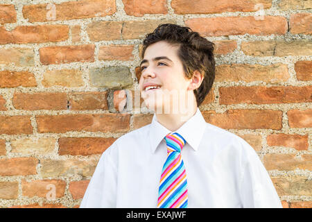 Handsome Caucasian boy leaning against an ancient brick wall while he is wearing a white shirt and a regimental tie with red, fuchsia, orange, blue, indigo, blue and white stripes Stock Photo