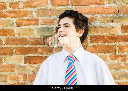 Handsome Caucasian boy leaning against an ancient brick wall while he is wearing a white shirt and a regimental tie with red, fuchsia, orange, blue, indigo, blue and white stripes Stock Photo