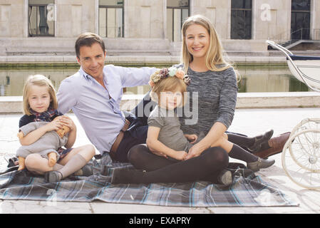 Family sitting on blanket in urban park, portrait Stock Photo