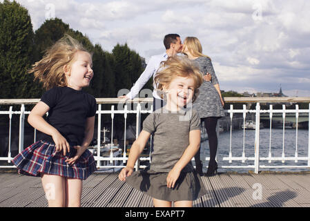 Little girls playing outdoors while their parents kiss in the background Stock Photo