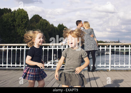 Little girls playing outdoors while their parents kiss in the background Stock Photo