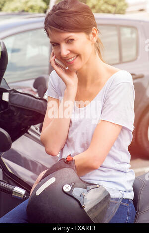 Woman sitting on parked motorcycle, talking on cell phone Stock Photo