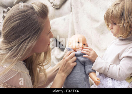 Mother and young daughter playing with baby doll together Stock Photo