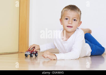 Boy lying on floor playing with toy truck Stock Photo