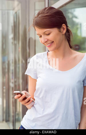 Woman using smartphone outdoors, smiling Stock Photo