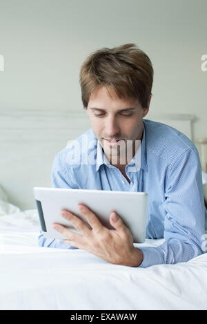 Man lying in bed using digital tablet Stock Photo