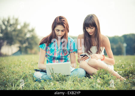 beautiful hipster young women sisters friends using tablet and smartphone in the park Stock Photo