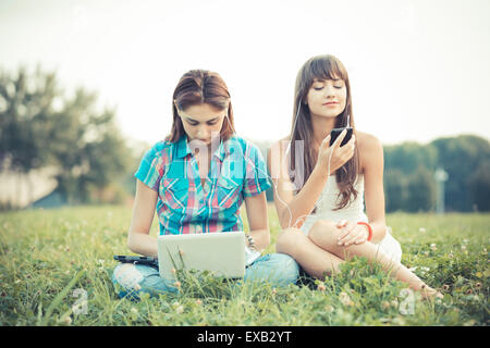 beautiful hipster young women sisters friends using tablet and smartphone in the park Stock Photo