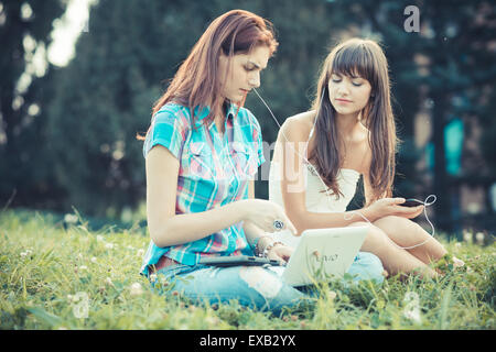 beautiful hipster young women sisters friends using tablet and smartphone in the park Stock Photo