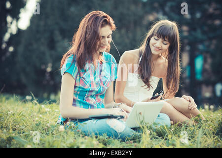 beautiful hipster young women sisters friends using tablet and smartphone in the park Stock Photo