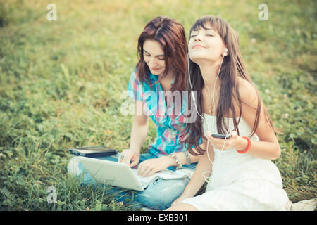 beautiful hipster young women sisters friends using tablet and smartphone in the park Stock Photo