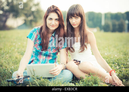 beautiful hipster young women sisters friends using tablet and smartphone in the park Stock Photo