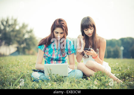 beautiful hipster young women sisters friends using tablet and smartphone in the park Stock Photo