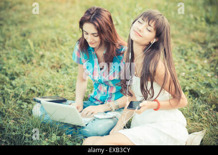 beautiful hipster young women sisters friends using tablet and smartphone in the park Stock Photo