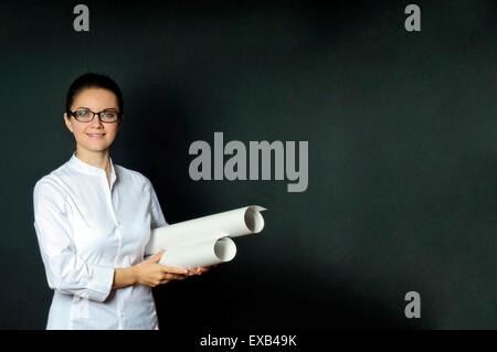 Studio portrait of an engineer woman in a white blouse with a stack of drawings, dark background with blank space Stock Photo