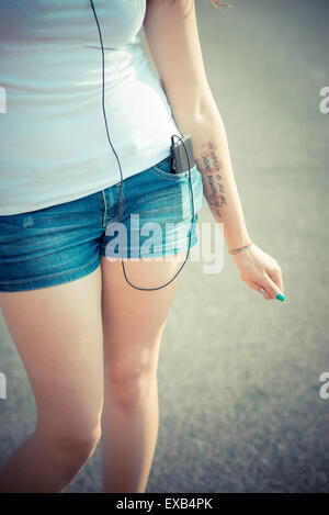 close up of young beautiful long curly hair hipster woman legs listening to music with smartphone in the city
