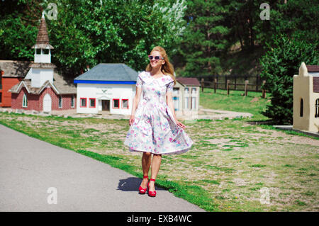 Young woman in a vintage dress, sunglasses and shoes walking down the street Stock Photo