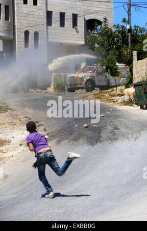 A small Palestinian boy throws a rock at an Israeli jeep that is spraying smelling chemical water in the West Bank village of Kafr Qaddum. One week before the end of Ramadan and the celebration of Eid al-Fitr, violence erupted in the West Bank Palestinian village of Kafr Qaddum. In Kafr Qaddum, protests were held inside the village against the Israeli occupation, which is part of the reason why so many people are not given travel permits to Jerusalem. Israeli soldiers tried to ambush protesters inside the village by camouflaging themselves in rubbish piles, however they did not arrest anyone. Stock Photo