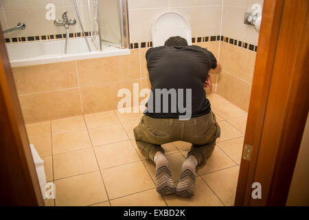 Rear View of a Drunk Young Man Vomiting in the Toilet at Home While in Kneeling Position. Stock Photo