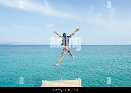 Young man jumping from the dock into the sea with his clothes on Stock Photo