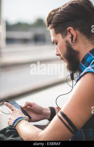 young handsome bearded hipster man using smartphone and listening music with earphones in the city Stock Photo
