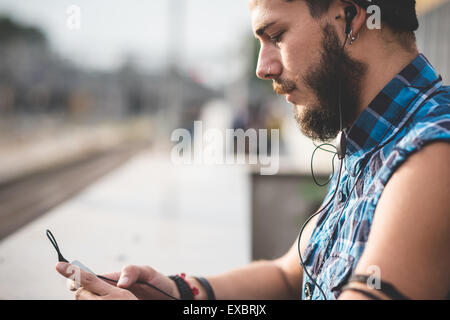 young handsome bearded hipster man using smartphone and listening music with earphones in the city Stock Photo