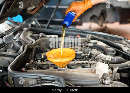 Mechanic topping up the oil in a car pouring a pint of oil through a funnel into the engine, close up of his hand and the oil Stock Photo