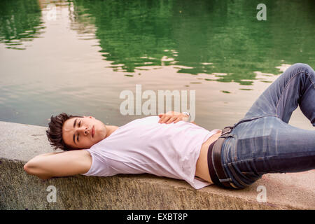 Handsome young man on a lake's shore or river banks in a sunny, peaceful day, lying down Stock Photo