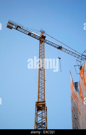 Yellow construction crane on building site with white Ad space on the top against blue sky. Stock Photo