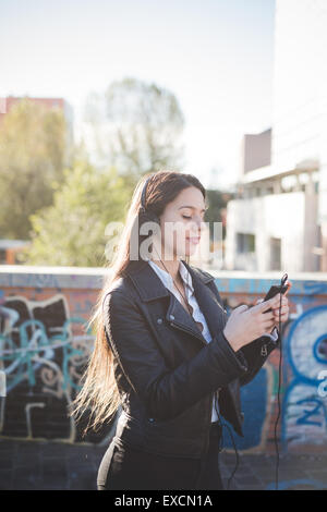 young beautiful long hair woman in town during sunset backlight listening to music with headphones