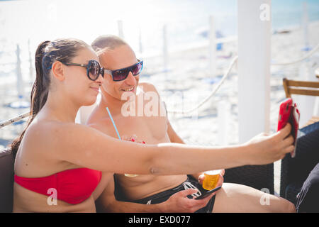young beautiful couple man and woman taking selfie at the beach bar in summertime Stock Photo