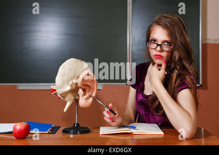 Excellent pupil sitting at a desk. On the table is a layout of the human ear, laptop, notebook and apple. Schoolgirl Stock Photo