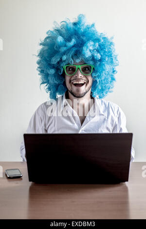 funny crazy young man with blue wig using notebook on the table Stock Photo