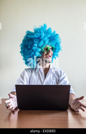 funny crazy young man with blue wig using notebook on the table Stock Photo