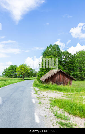 Old Worn Red Barn Near Road With a Blue Cloudy Sky Stock Photo